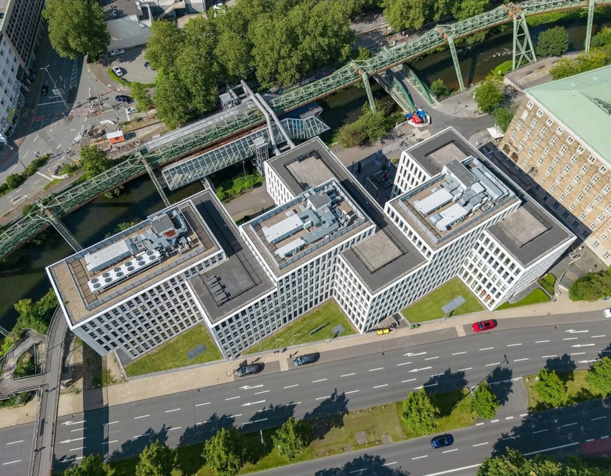 Senkrechte Drohnenaufnahme eines Bürokomplexes mit Dachtechnik, Schwebebahn und Fluss