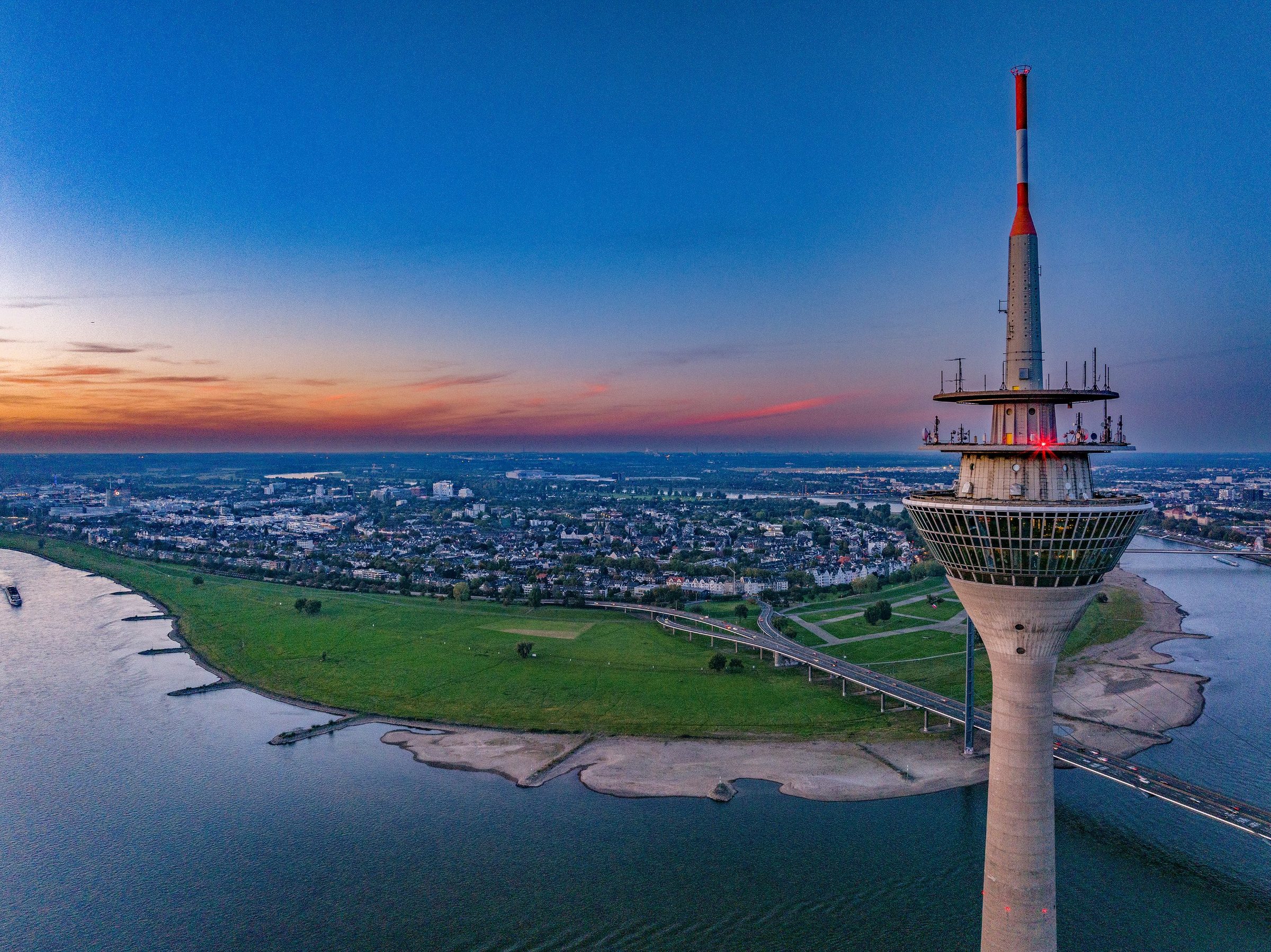 Drohnenaufnahme des Düsseldorfer Rheinturms in der Blauen Stunde mit Blick über Rheinbogen und Stadt
