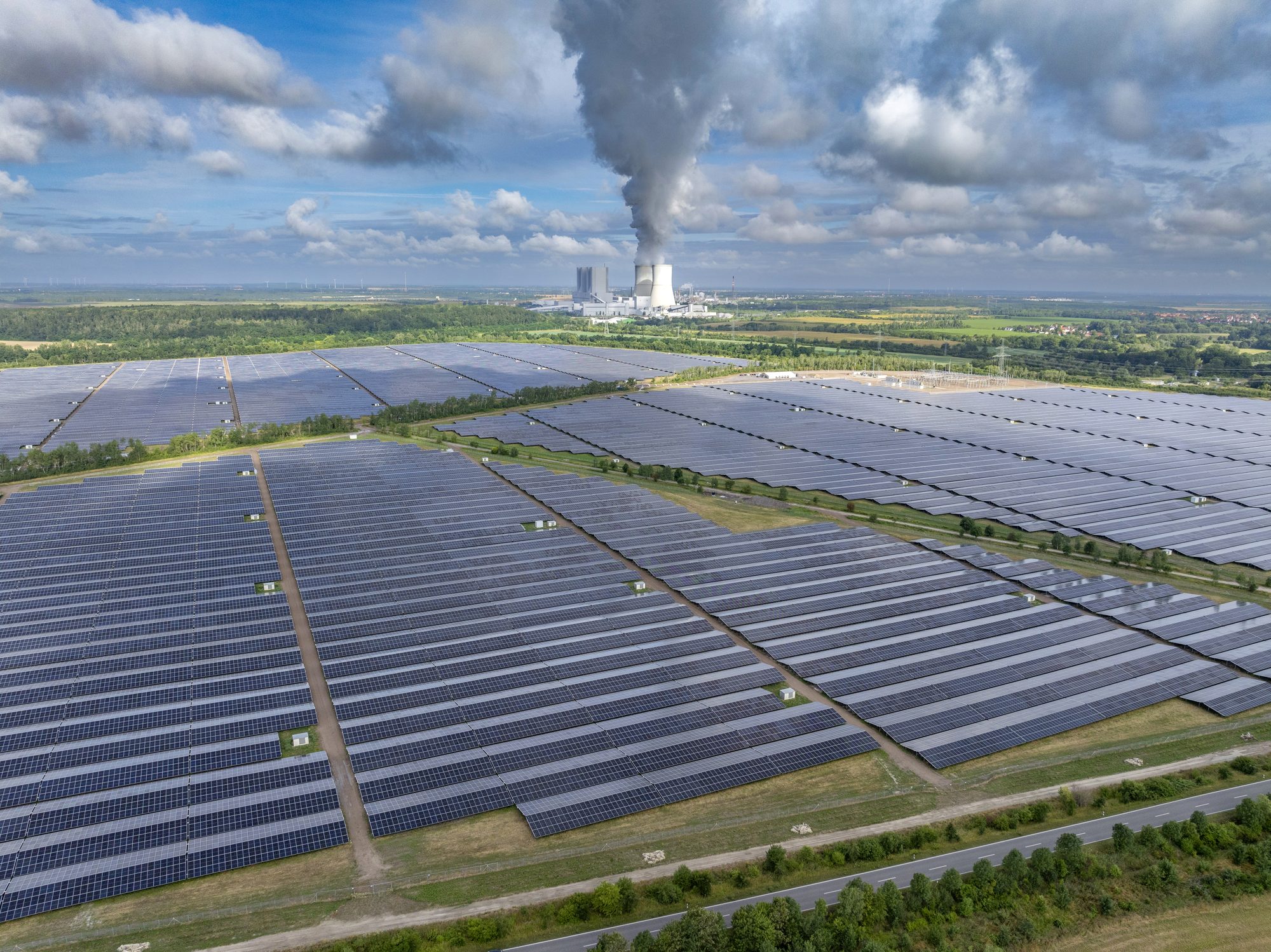 Luftaufnahme des Solarparks Witznitz bei Leipzig mit endlosen Modulreihen, Wartungswegen und einem Kraftwerk am Horizont